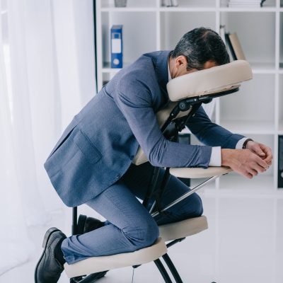 businessman in suit sitting in massage chair at office