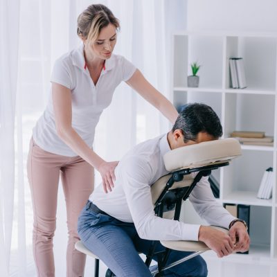 masseuse doing back massage for businessman at office