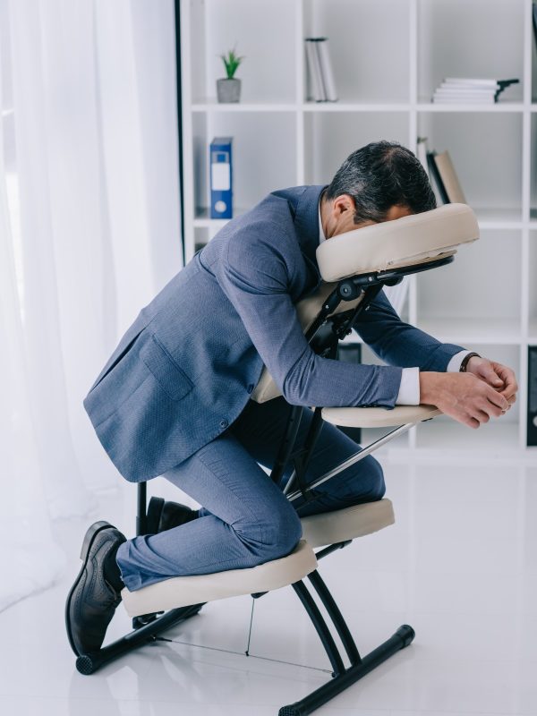 businessman in suit sitting in massage chair at office