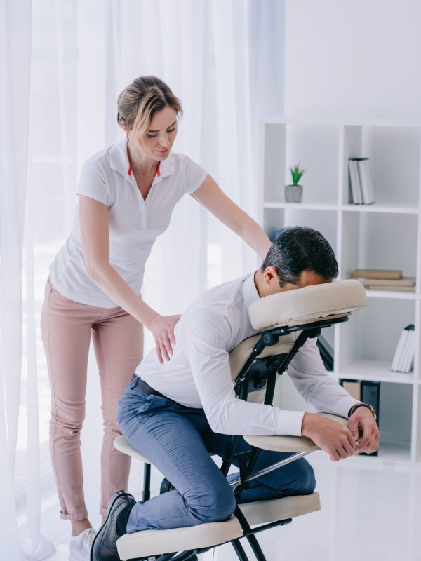 masseuse doing back massage for businessman at office